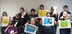 Joukko nuoria seisoo kahdessa rivissä, viidellä on kädessään tekemänsä grafiikan työ, lopuilla on malli suunnitteilla olevasta reliefistä.