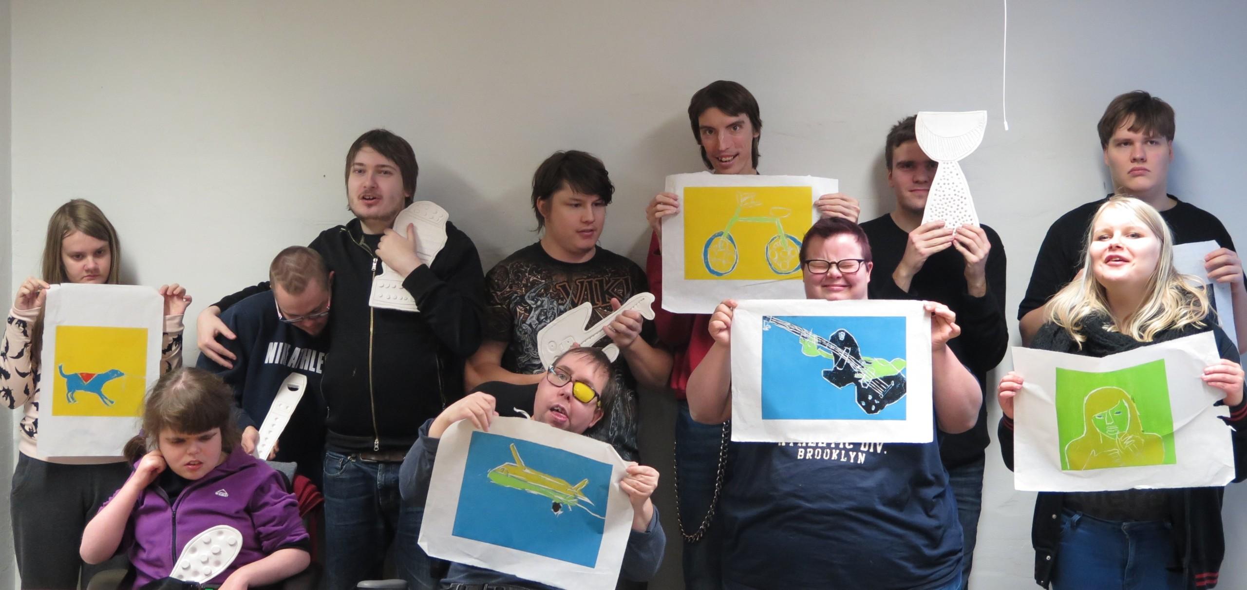 Joukko nuoria seisoo kahdessa rivissä, viidellä on kädessään tekemänsä grafiikan työ, lopuilla on malli suunnitteilla olevasta reliefistä.