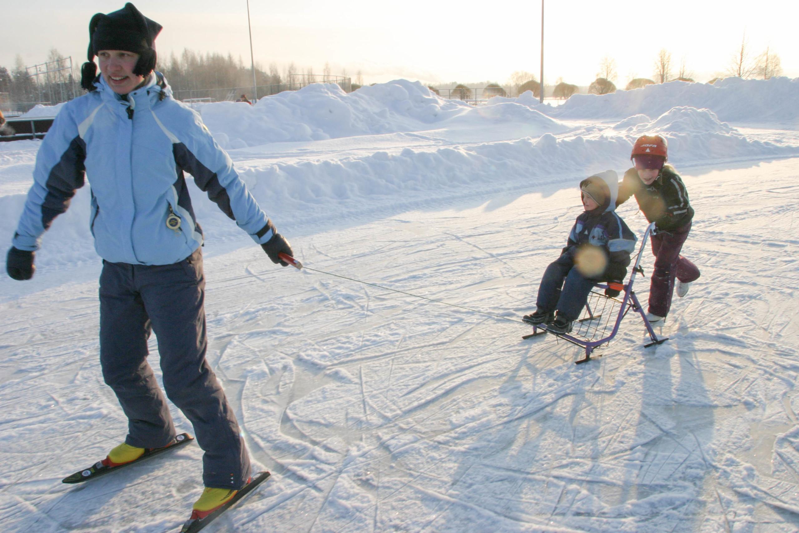 Symbolikuvassa nainen vetää vammaista lasta jäällä. Lapsi istuu suksukelkassa ja toinen lapsi työntää häntä.
