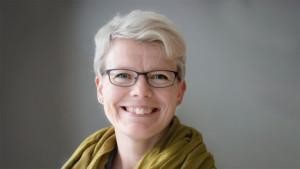 Iloinen, lyhyttukkainen, silmälasipäinen nainen.