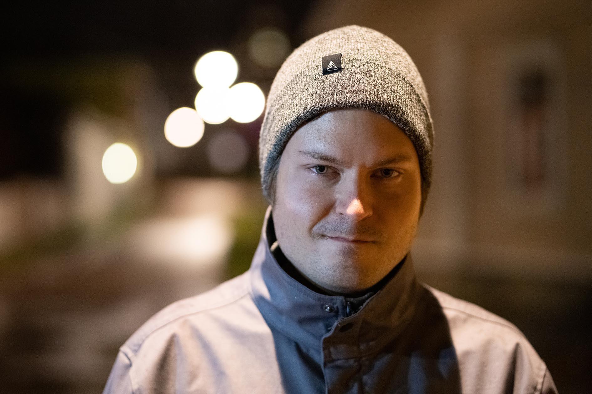 Nuori mies hymyilee ulkona, pipo päässä.